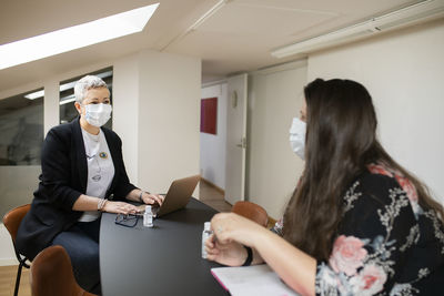 Female coworkers with protective face masks talking in office