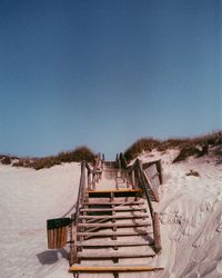 Staircase on beach against clear blue sky