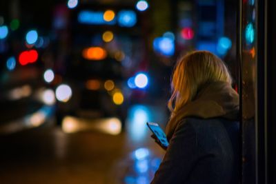 Side view of woman using phone on street at night