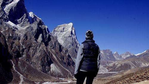 Rear view of man standing on rock against blue sky