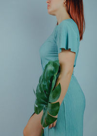 Midsection of woman holding leaf while standing blue background