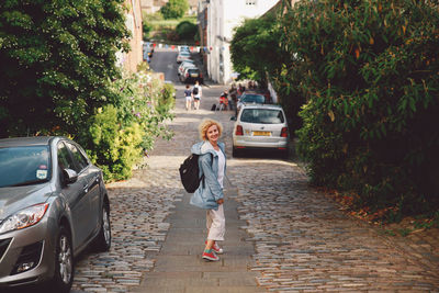 Happy young woman standing on street amidst trees