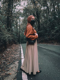 Side view of woman standing on road in forest