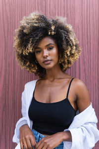 Confident african american female wearing stylish casual outfit looking at camera standing against colorful door