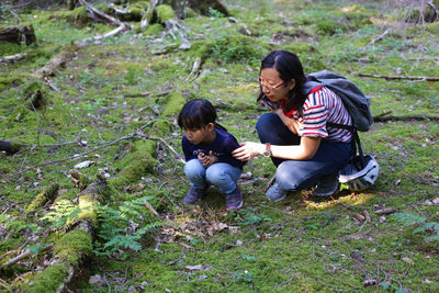 Mother and daughter squatting on forest floor filled with moss and checking for insects
