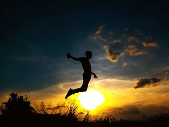 Silhouette of girl jumping on field at sunset