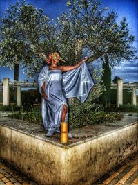 Rear view of woman sitting by tree against sky