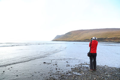 Rear view of woman photographing sea against clear sky