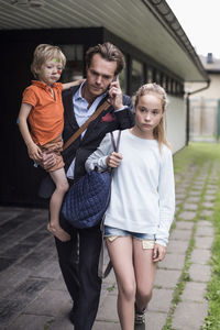 Businessman using mobile phone while walking with children at yard