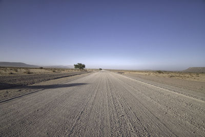 Road amidst field against clear blue sky