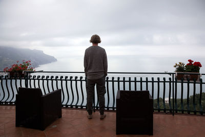 Rear view of man standing on railing against sky