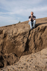 Rear view of man sitting on rock against sky