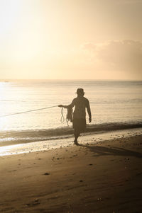 Silhouette woman walking at beach against sky during sunset