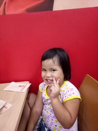 Portrait of a smiling girl showing peace sign while sitting in restaurant 