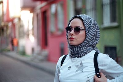 Woman wearing sunglasses and scarf standing against building