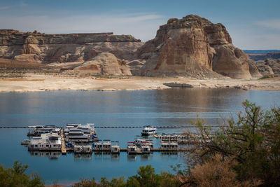 Boats docked on lake powell, utah with sandstone cliffs and beach in background.