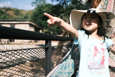 Girl pointing while standing by fence