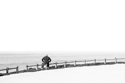 Rear view of man standing by lake against clear sky