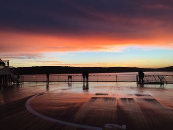 Silhouette people by railing against sky during sunset