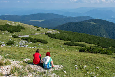 Rear view of men sitting on mountain against mountains