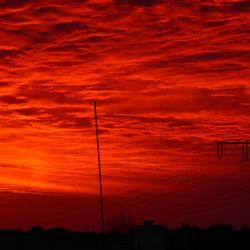 Low angle view of silhouette electricity pylon against dramatic sky