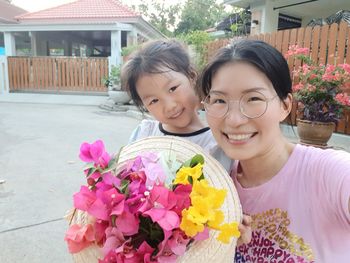 Portrait of happy girl with pink flowers against plants