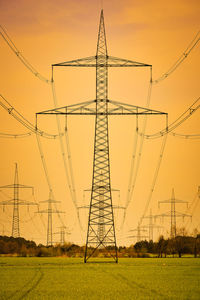 Low angle view of electricity pylon on field against sky during sunset