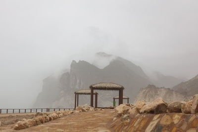 Gazebos by mountains against sky in foggy weather