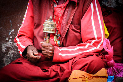 Midsection of man holding prayer wheel while sitting outdoors