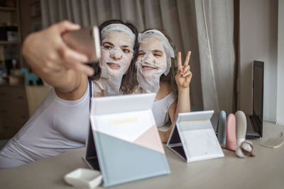 Mother and daughter with facial mask doing selfie at home