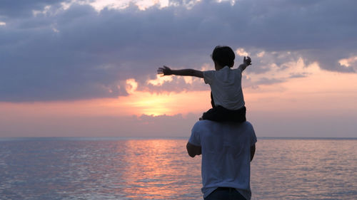 Rear view of man standing in sea against sunset sky