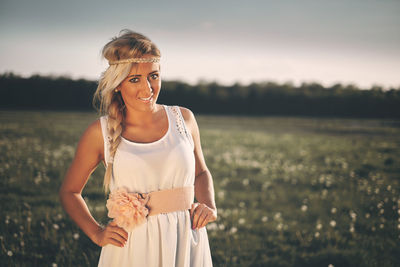 Portrait of young woman standing on grassy field during sunset