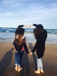 Rear view of women making heart shape using hands at beach