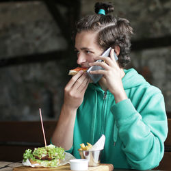 Young man eating food at restaurant while talking on phone