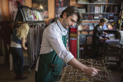 Male worker making chaise longue with female colleagues working in background at workshop