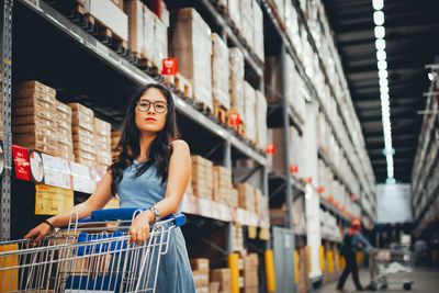 Portrait of woman with shopping cart standing at supermarket