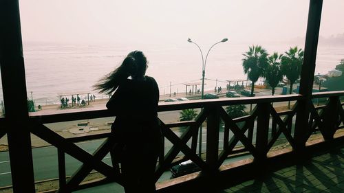 Woman standing on table by sea against clear sky