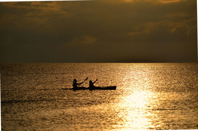 People on canoe boat on sea against sky during sunset