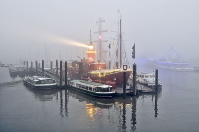 Germany, hamburg, lightship and various boats moored in foggy harbor