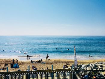 People on beach against clear blue sky