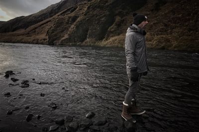 Side view of man standing in river by mountain