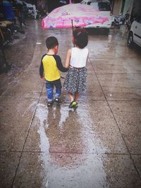 Rear view of boys walking on wet road during rainy season