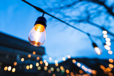 A light bulb from a string of lights in focus with an outdoor street background