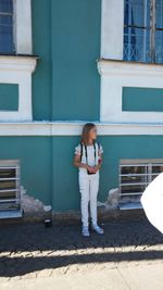 A full-length girl standing on the pedestrian path near the building