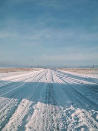 Tire tracks on snow covered field against sky