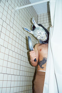 Portrait of shirtless man wearing mask standing in bathroom
