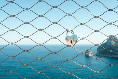 Heart shape love lock hanging on fence against mediterranean sea