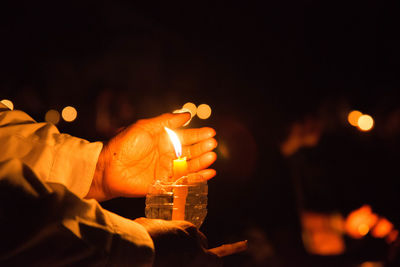 Midsection of man holding illuminated candles against fire at night