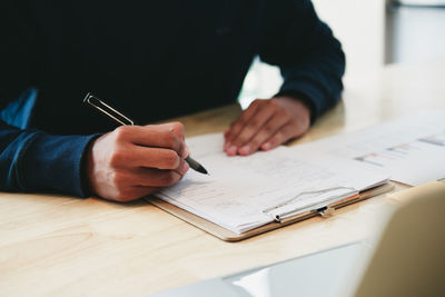 Midsection of man holding paper while sitting on table