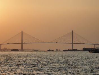 Suspension bridge over sea against sky during sunset